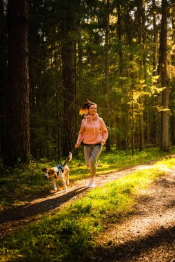 Genç bir kadın ve köpek ormanda birlikte koşuyorlar. Neşeli dişi, evcil hayvanıyla dışarıda egzersiz yapıyor. Etkin insanlar konsepti.