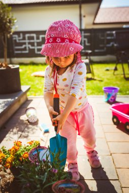 2-3 yaşlarında bir çocuk annesine bahçe işlerinde yardım ediyor. Baharda saksıya çiçek ekiyorum..