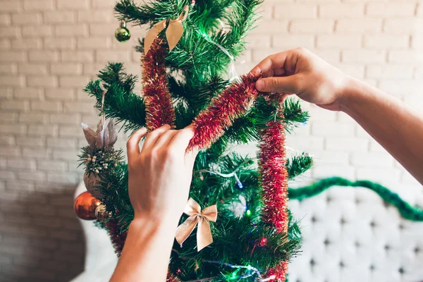 Hände schmücken Weihnachtsbaum mit rotem Lametta — Stockfoto