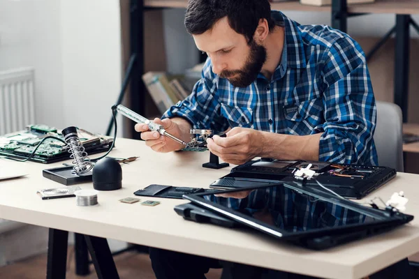 Engineer soldering microcircuit though magnifier — Stock Photo, Image