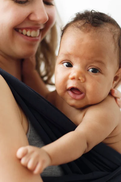 Lächelndes entzückendes Baby mit glücklicher Mutter im Tragetuch — Stockfoto