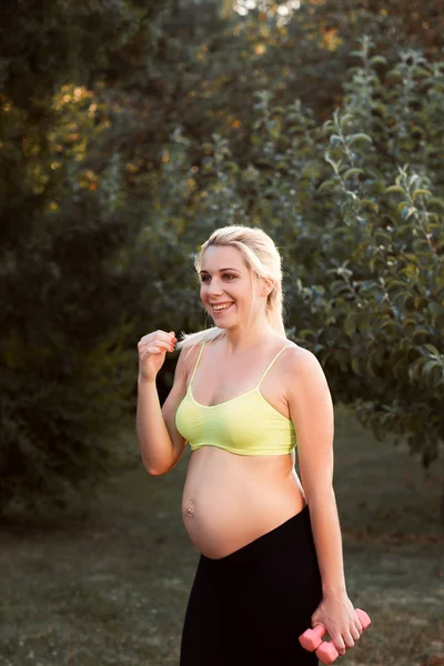 Smiling pregnant fitness lady outdoor, free space