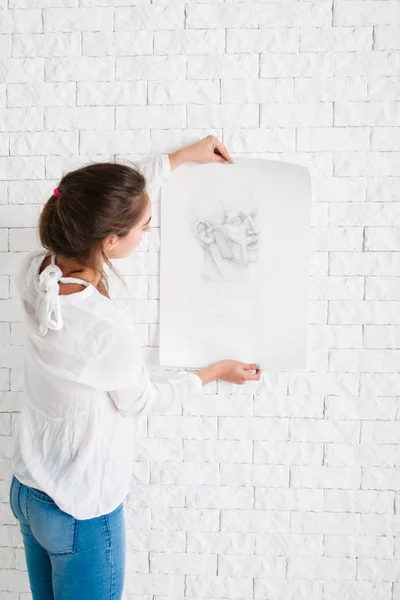 Woman looking at pencil portrait against wall — Stock Photo, Image