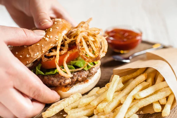 Hand med hamburgare från träbricka — Stockfoto