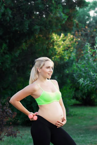 Sorridente donna incinta in posa con i manubri — Foto Stock
