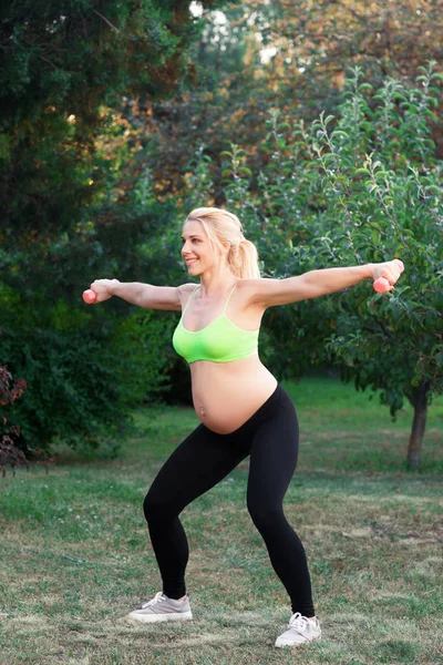 Těhotná blondýna v podřepu s činkami venkovní — Stock fotografie
