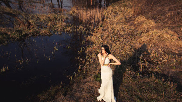 Bride with long hair and lake. View from above wedding shoot of beautiful girl in white dress on gorgeous autumn nature background