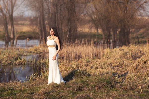 Bride with long hair and lake. Wedding shoot of beautiful girl in white dress on gorgeous autumn nature background
