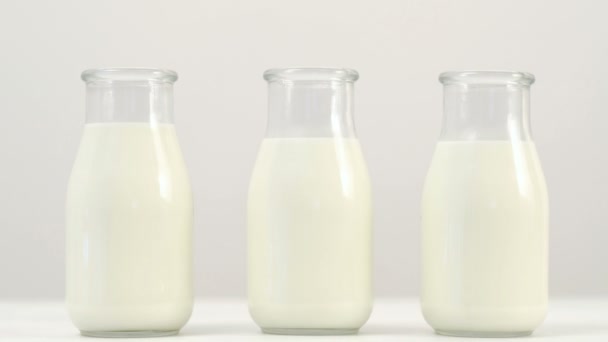 Tres botellas de leche fondo blanco diapositiva disparo — Vídeo de stock