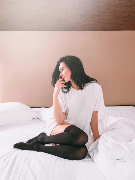 Dreamy pensive woman t shirt black stockings bed — Stock Photo, Image
