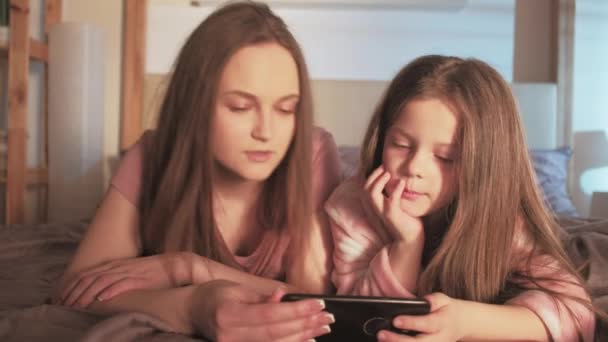Educación en línea joven madre hija teléfono cama — Vídeo de stock
