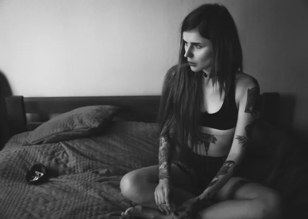 Junge tätowierte Frau mit langen Haaren raucht im Schlafzimmer — Stockfoto