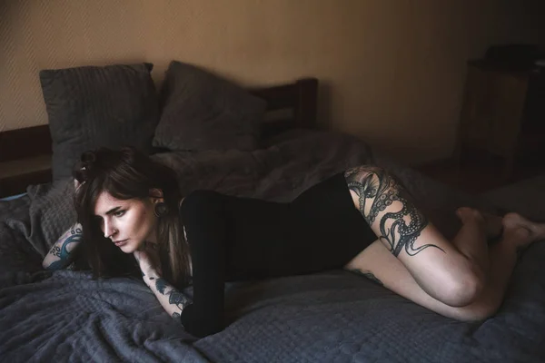 Junge tätowierte Frau mit langen Haaren posiert im Schlafzimmer Stockbild