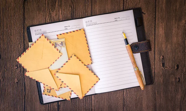 Una mesa de madera con un cuaderno, sobres y otros artículos de papelería . — Foto de Stock