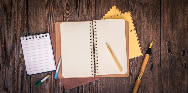 Una mesa de madera con un cuaderno, sobres y otros artículos de papelería . —  Fotos de Stock