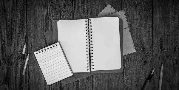 Cuaderno con sobre una mesa de madera. Blanco y negro. Vista superior —  Fotos de Stock