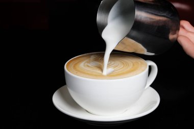 Kapuçino krem dökme. Siyah arka plan üzerine büyük beyaz Kupası.