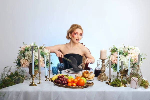 Modelo loira de moda com maquiagem colorida sentada atrás de mesa decorada festiva e corte de sapato de camurça — Fotografia de Stock