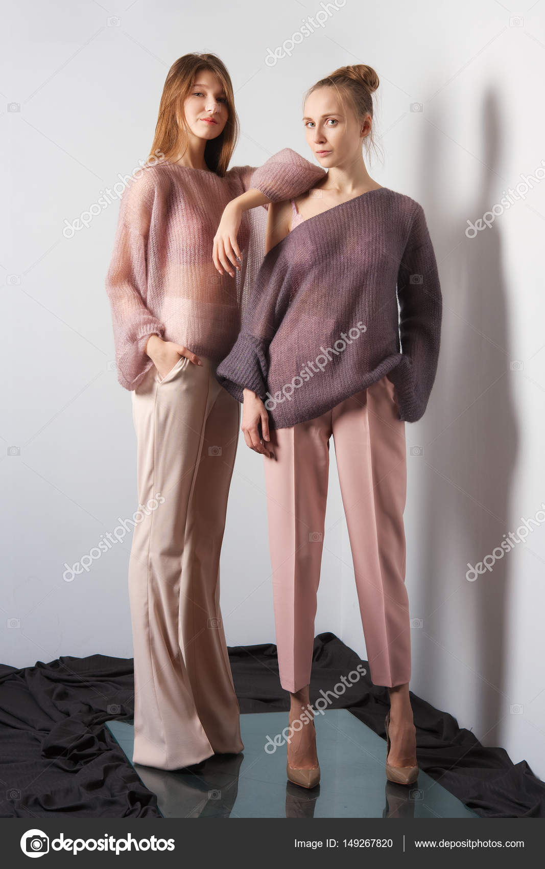 Two pretty girls in thin angora sweater and pants posing near the wall Stock Photo boomeart 149267820