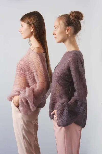 Дві красиві дівчата в тонкому ангорському светрі і штани позують біля стіни — стокове фото