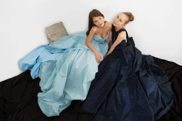 Two fashion models in fluttering dress on the floor. Flowing hemline.