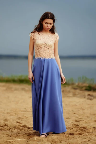 Calmo modelo de moda solitário andando na areia em um dia nublado. Romântico, suave, místico, imagem de uma menina em saia azul longa e blusa de renda . — Fotografia de Stock