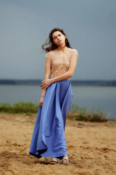 Calm lonely fashion model walking on the sand in a cloudy day. Romantic, gentle, mystical, image of a girl in long blue skirt and lace blouse.