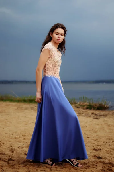 Calma modelo de moda solitaria caminando sobre la arena en un día nublado. Romántica, suave, mística, imagen de una chica en falda larga azul y blusa de encaje . — Foto de Stock