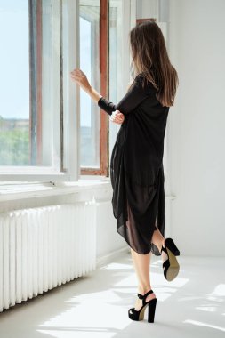 Pencerenin yanındaki elbise içinde tanınmayan kız arkadan görünüm.