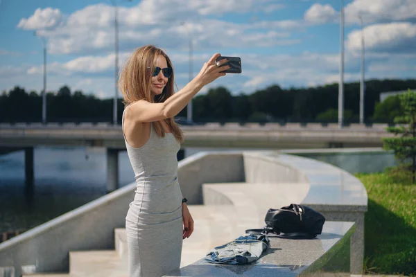 สาวนักท่องเที่ยวที่น่าสนใจ กําลังถ่ายเซลฟี่กับฝั่งแม่น้ํา บนพื้นหลังในสวนสาธารณะ — ภาพถ่ายสต็อก
