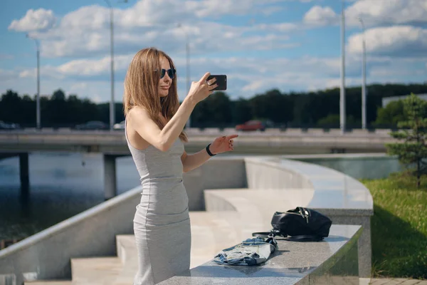 Atrakcyjnej dziewczyny co selfie z brzegu rzeki na tle w parku miejskim — Zdjęcie stockowe