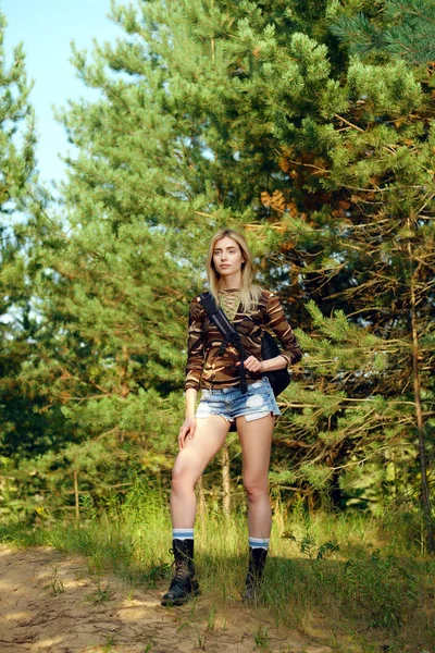 Attraktiva flicka i camo skjorta, jeansshorts med ryggsäck på vandring trail i skogen — Stockfoto
