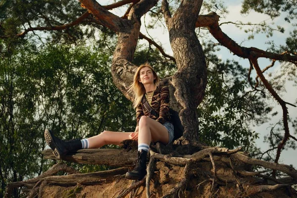 Menina turística atraente sentado na raiz da árvore — Fotografia de Stock