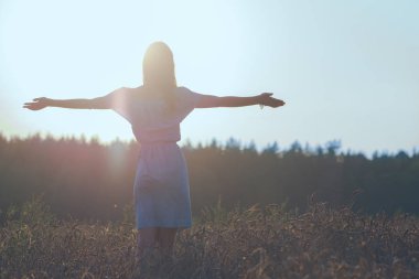 Gün batımında buğday alanında güzel genç bayan. Güneşli akşam zevk rahat mavi elbiseli kız