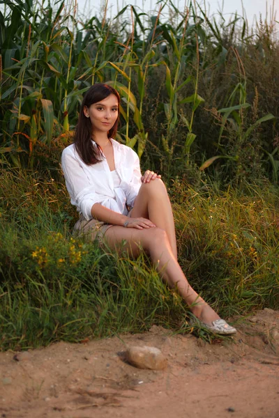 Chica bonita sentada al borde de la carretera del campo en la puesta del sol — Foto de Stock