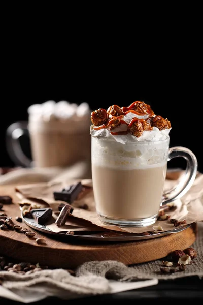 Komposisi dengan dua gelas cappuccino diatapi dengan krim kocok dan disajikan dengan biji kopi dan coklat pada papan kayu di atas latar belakang hitam — Stok Foto