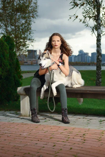 Şehir Parkı husky köpek ile oturan kız. Köpek bir bankta.