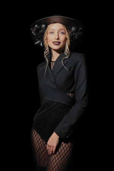Modelo de moda sexy en vestido de rejilla y sombrero con flores posando en un ambiente oscuro — Foto de Stock
