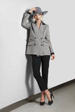 Güzel moda model gri duvara yakın poz çiçekli ceket, pantolon ve geniş ağzına kadar şapkalı