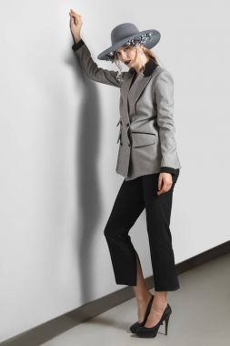 Güzel moda model gri duvara yakın poz çiçekli ceket, pantolon ve geniş ağzına kadar şapkalı