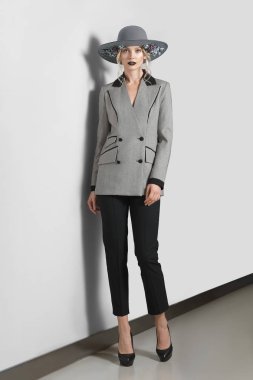 Güzel moda model gri duvara yakın poz çiçekli ceket, pantolon ve geniş ağzına kadar şapkalı