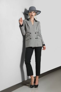 Güzel moda model gri duvara yakın poz çiçekli ceket, pantolon ve geniş ağzına kadar şapkalı