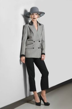 Güzel moda model gri duvara yakın poz çiçekli ceket, pantolon ve geniş ağzına kadar şapkalı