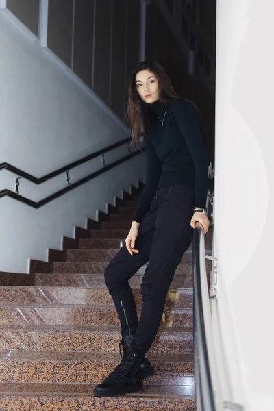 Chica seria en pantalones militares, botas ásperas y suéter posando en las escaleras — Foto de Stock
