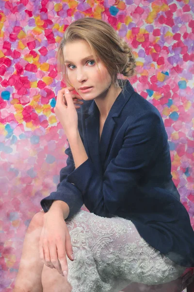 Retrato de linda chica en chaqueta azul y falda de encaje sentado en silla sobre fondo de flor vibrante —  Fotos de Stock