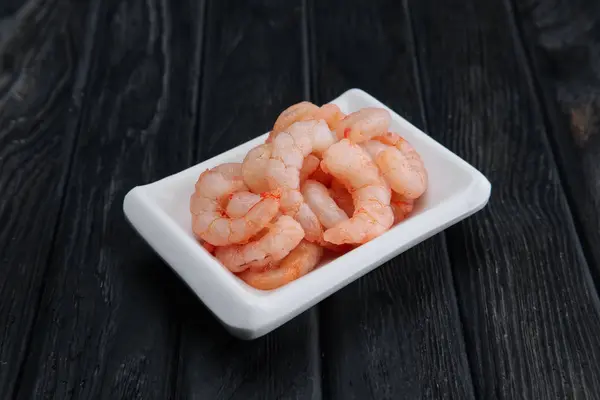 Petites crevettes pelées bouillies dans une petite assiette sur fond de bois foncé — Photo