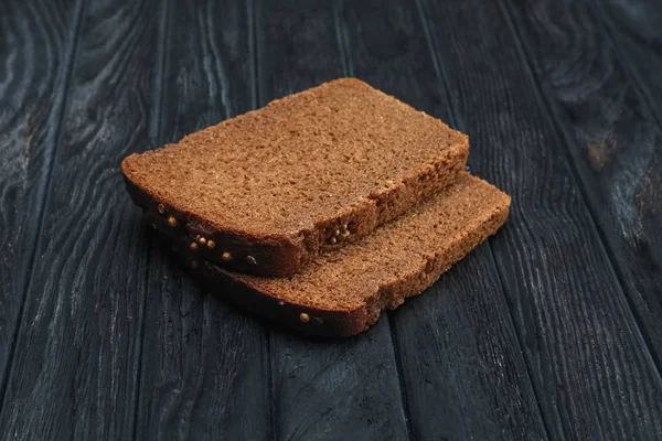 Två bitar av brunt bröd på mörka träbord — Stockfoto