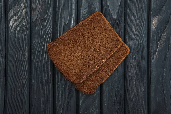 Dos piezas de pan marrón sobre una mesa de madera oscura. Vista superior . — Foto de Stock