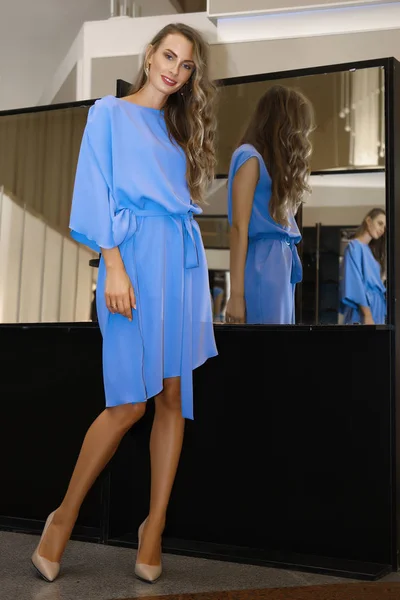 Красивая девушка в голубом платье рядом с зеркалом с несколькими отражениями — стоковое фото