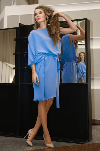 Красивая девушка в голубом платье рядом с зеркалом с несколькими отражениями — стоковое фото